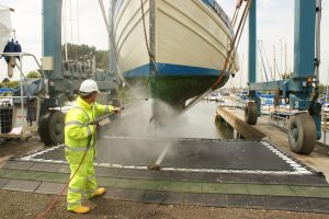 A person in protective clothing pressure washing the hull of a boat