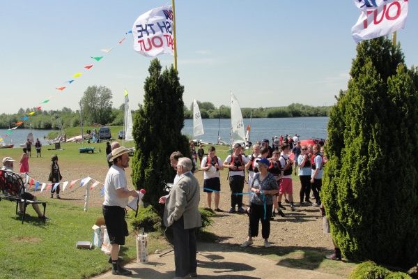 People standing on a path beside water with sailing dinghies