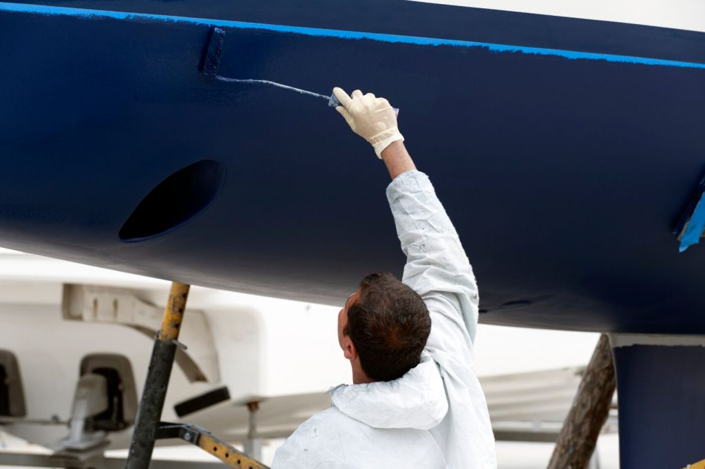 A person applying antifoul paint to the hull of a boat
