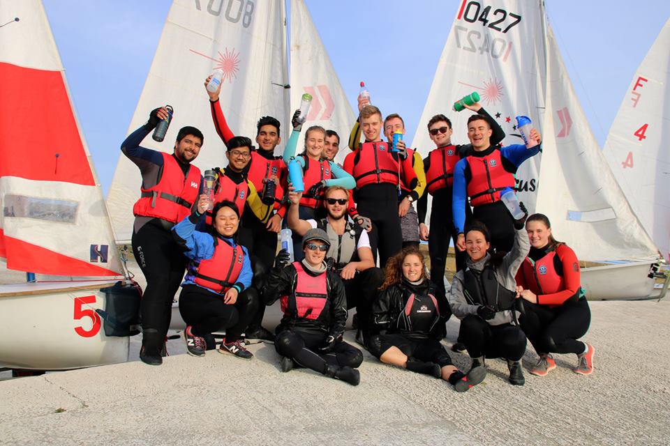 A group of sailors holding up their reusable water bottles in front of their boats.