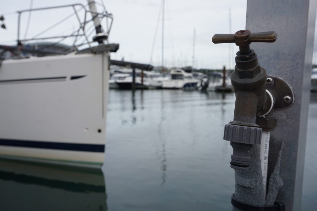 Water tap on a pontoon with the bow of a yacht in the background