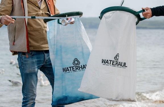 Two people hold recycled Waterhaul litter bags on a beach