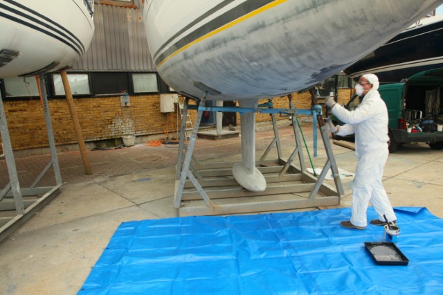 A man in protective clothing applying paint to a boat.