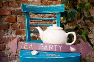 A white tea pot on a chair with a arrow directing visitors to the Tea Party