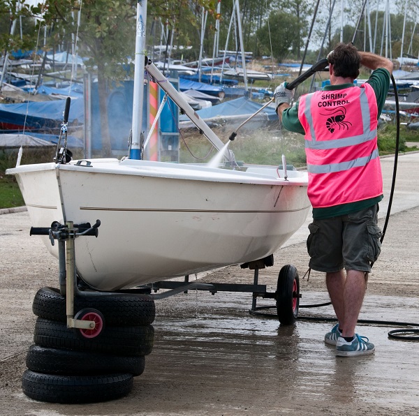 A man is washing down a dinghy with a pressured hose.