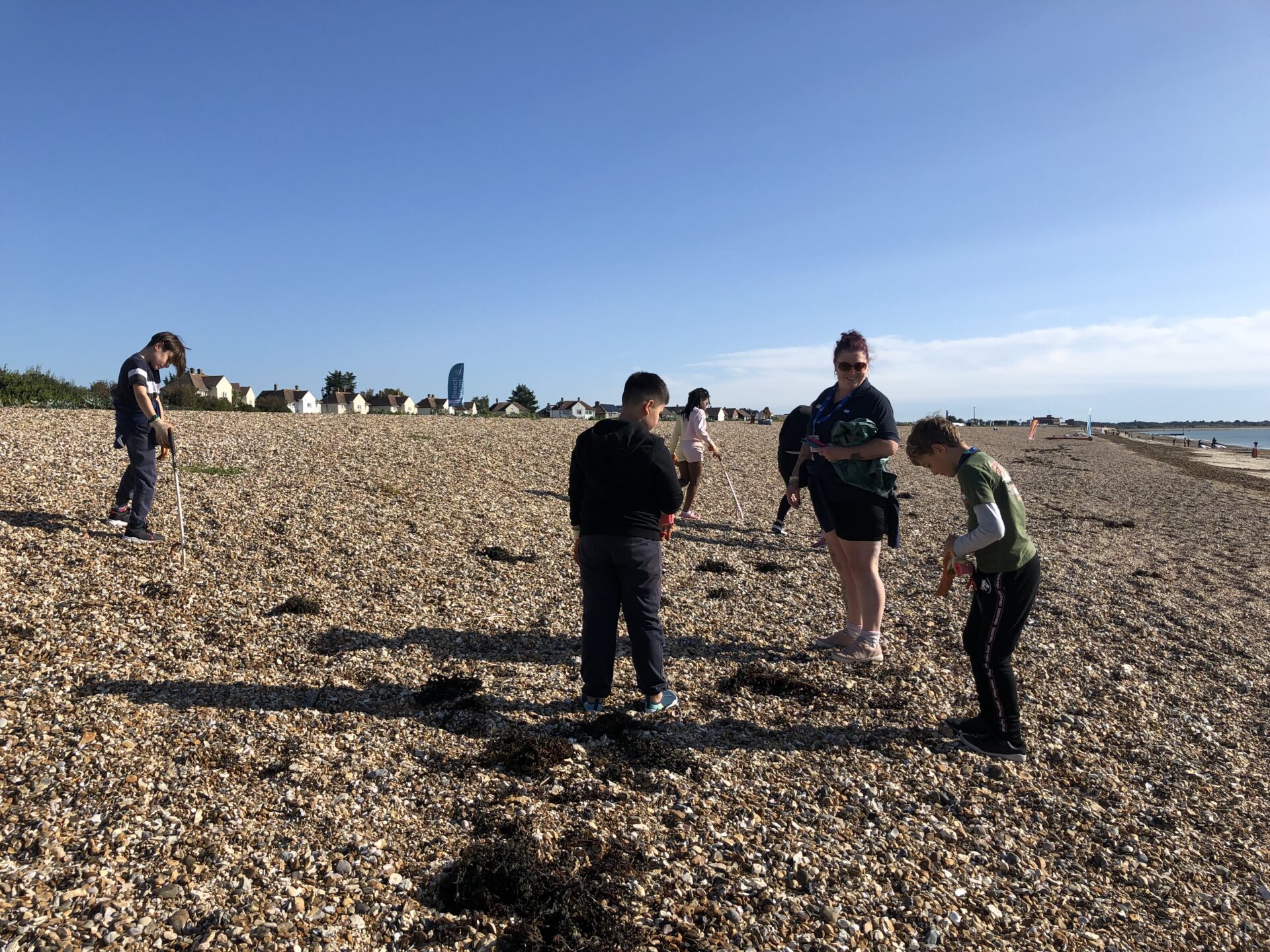 A group of children are walking along a beach with litter pickers