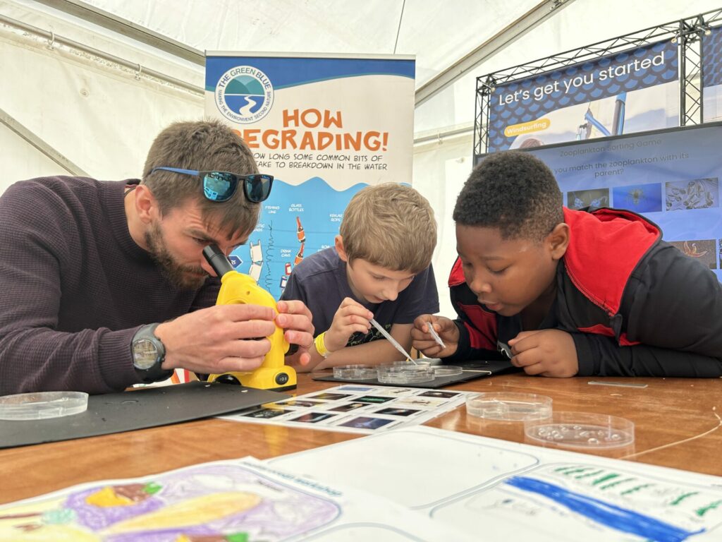 Two boys and a man are looking at specimen using magnifying tools
